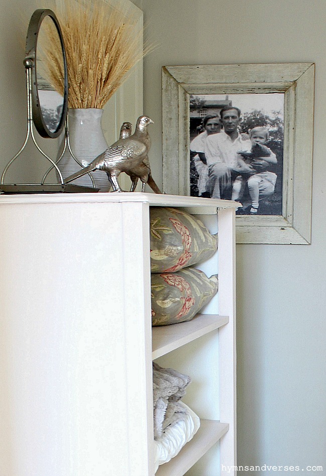 Old photograph in white picture frame close to cabinet with pillows and wheat in a pitcher and mirror