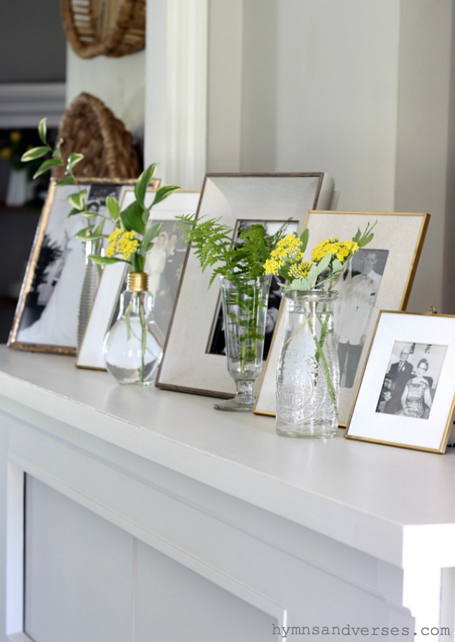 Framed photos on piano with flowers and greens in tiny vases. 