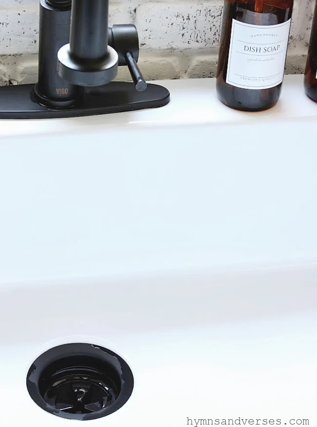 White fireclay farmhouse sink with black faucet and drain