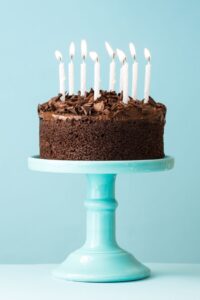 chocolate birthday cake with white candles on a blue pedestal